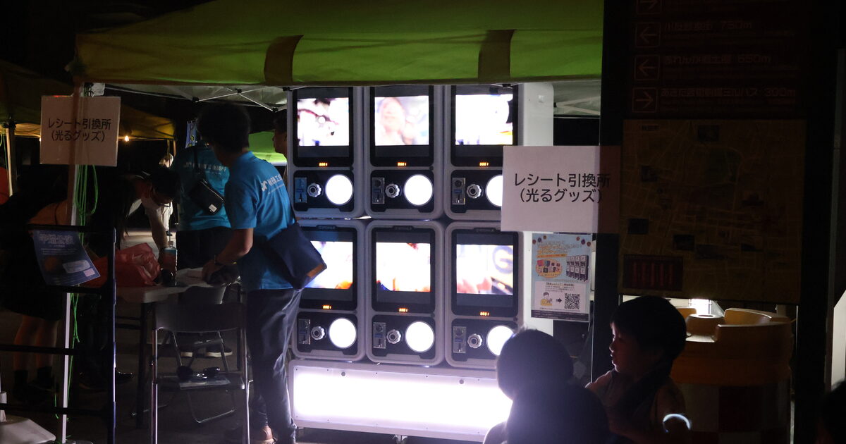 夜のイベントでライトアップされたデジタルガチャに集まる来場者