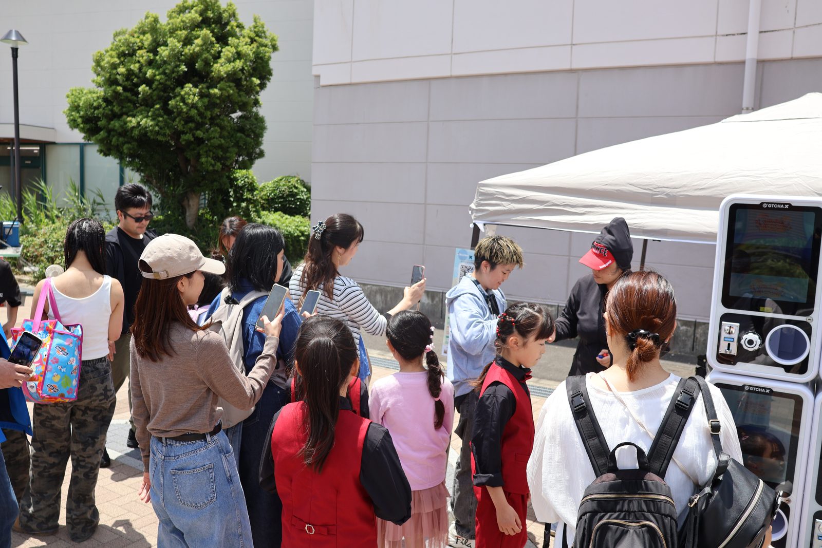 A crowd of visitors gathered around a digital-signage gacha machine